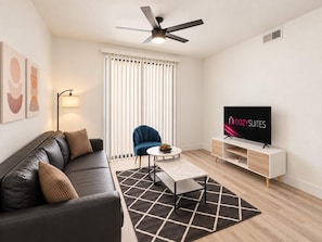 Ein modernes Wohnzimmer mit einer Couch, einem blauen Sessel, einem Couchtisch, einem Fernseher und einem Deckenventilator.