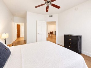 A bedroom with a bed, a ceiling fan, a dresser, and a door leading to a dining area. - CozySuites Glendale - Westgate w pool! 2BR 2BA (Glendale)
