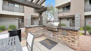 An outdoor patio with a grill and seating area, surrounded by stone walls and a metal fence. - CozySuites Glendale - Westgate w pool! 2BR 2BA (Glendale)