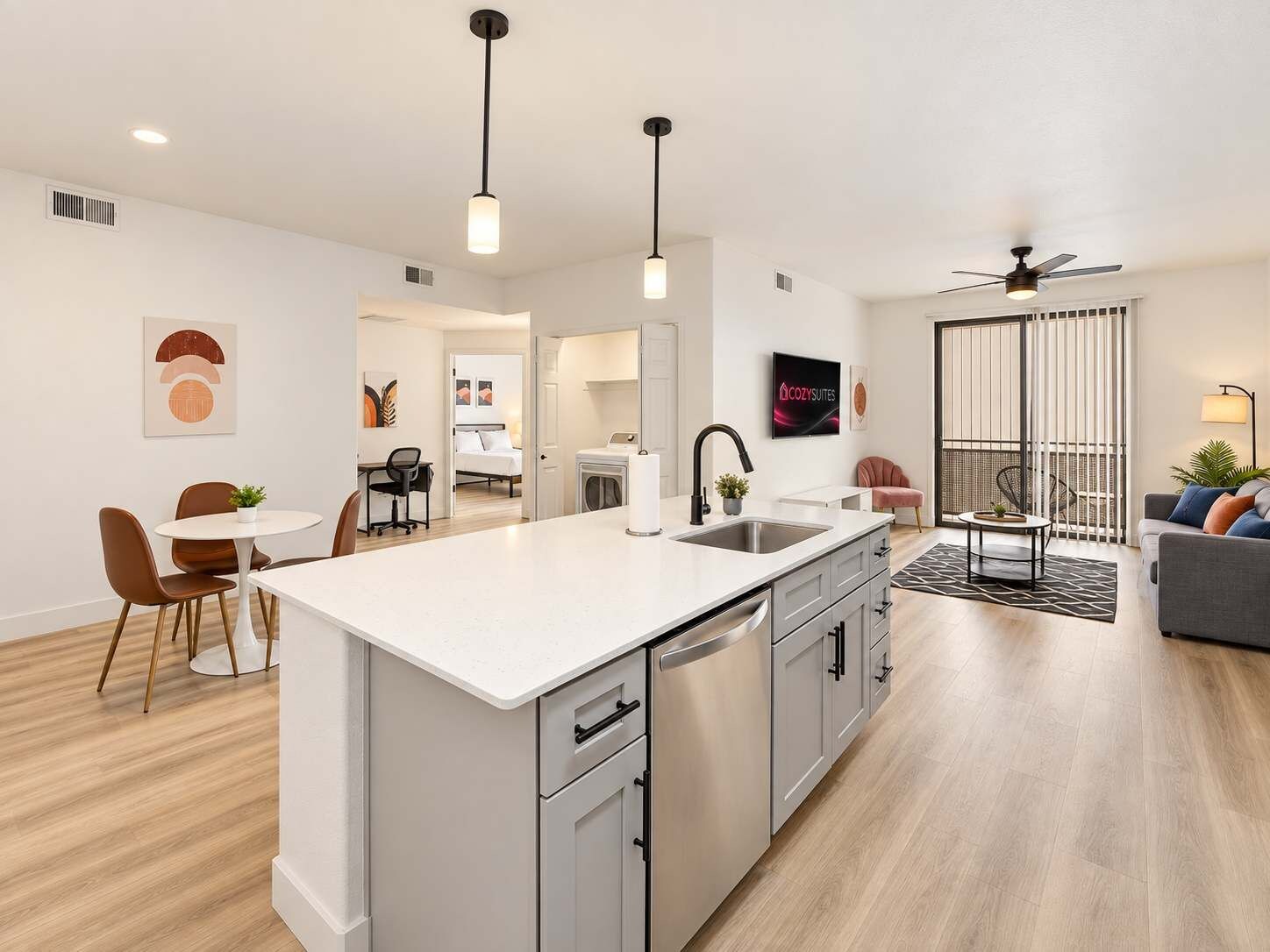 A modern kitchen with a central island, a dining area with chairs, a sofa, and a ceiling fan.