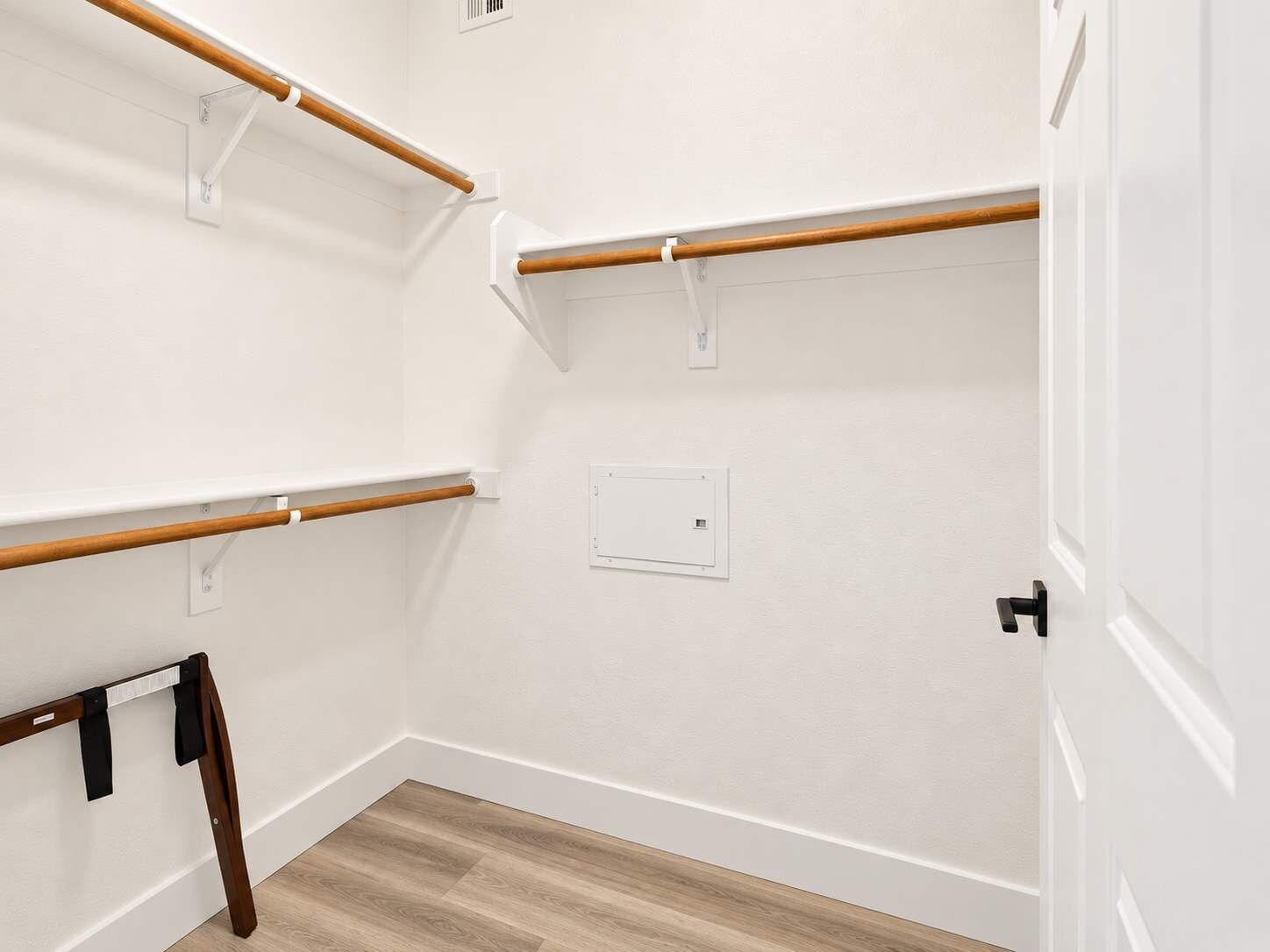 A room with white walls, a wooden floor, and a door with a black handle.