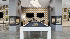 A modern indoor pool table with a geometric patterned wall in the background, a flat-screen TV mounted above it, and a minimalist ceiling design. - CozySuites Glendale - Westgate w pool! 2BR 2BA (Glendale)