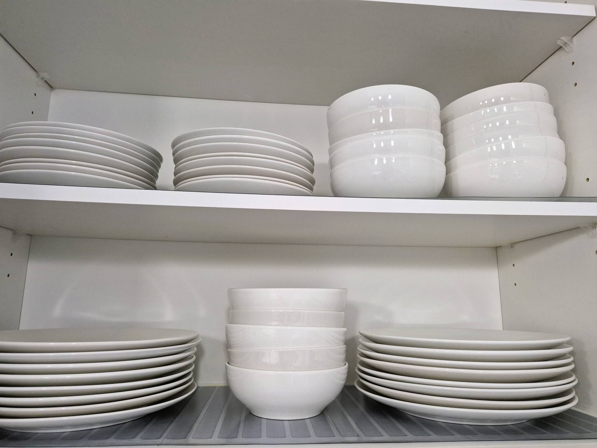 A storage area with white shelves holding stacks of plates and bowls.