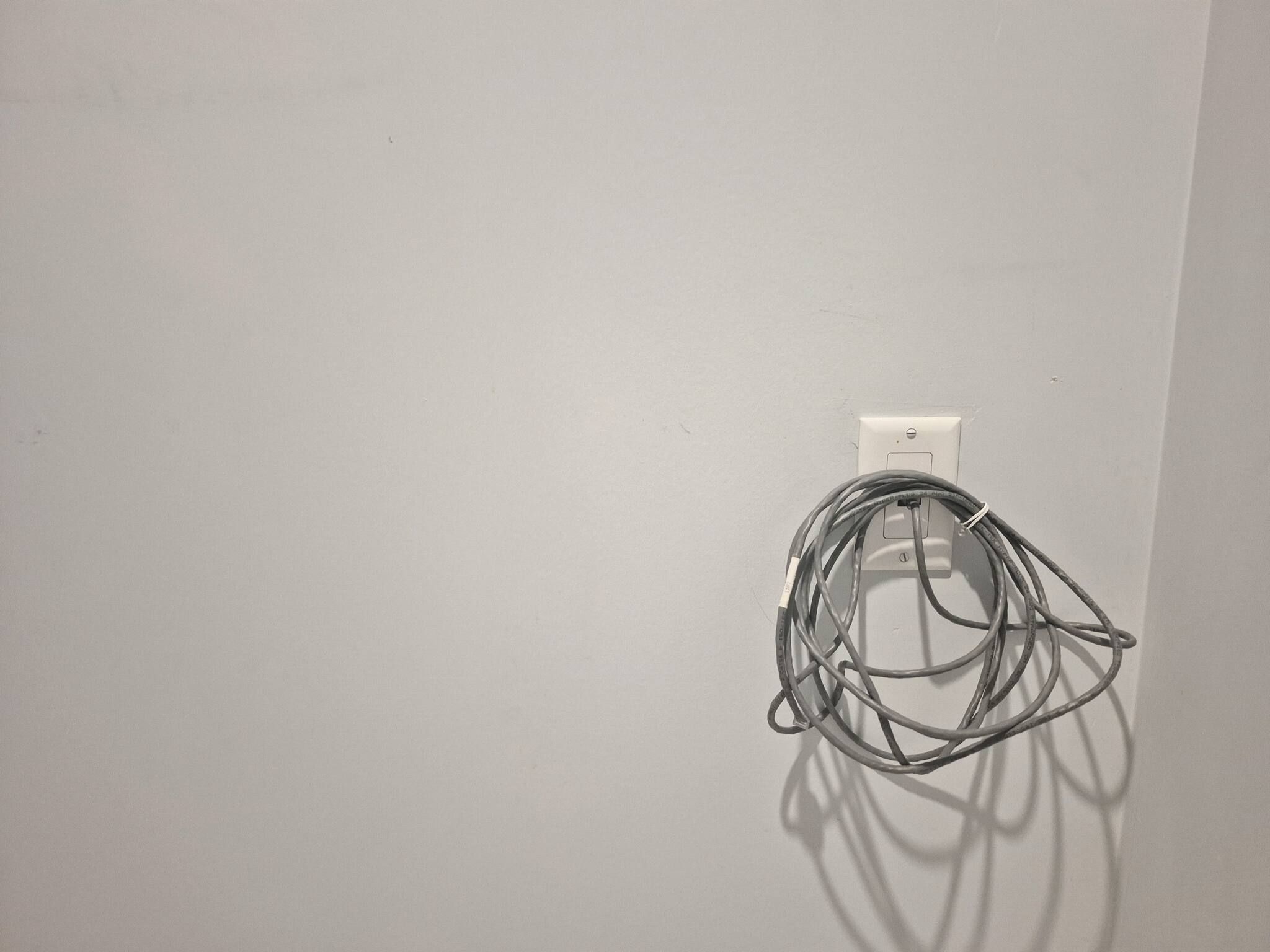 Pared blanca con un enchufe y un cable enrollado.