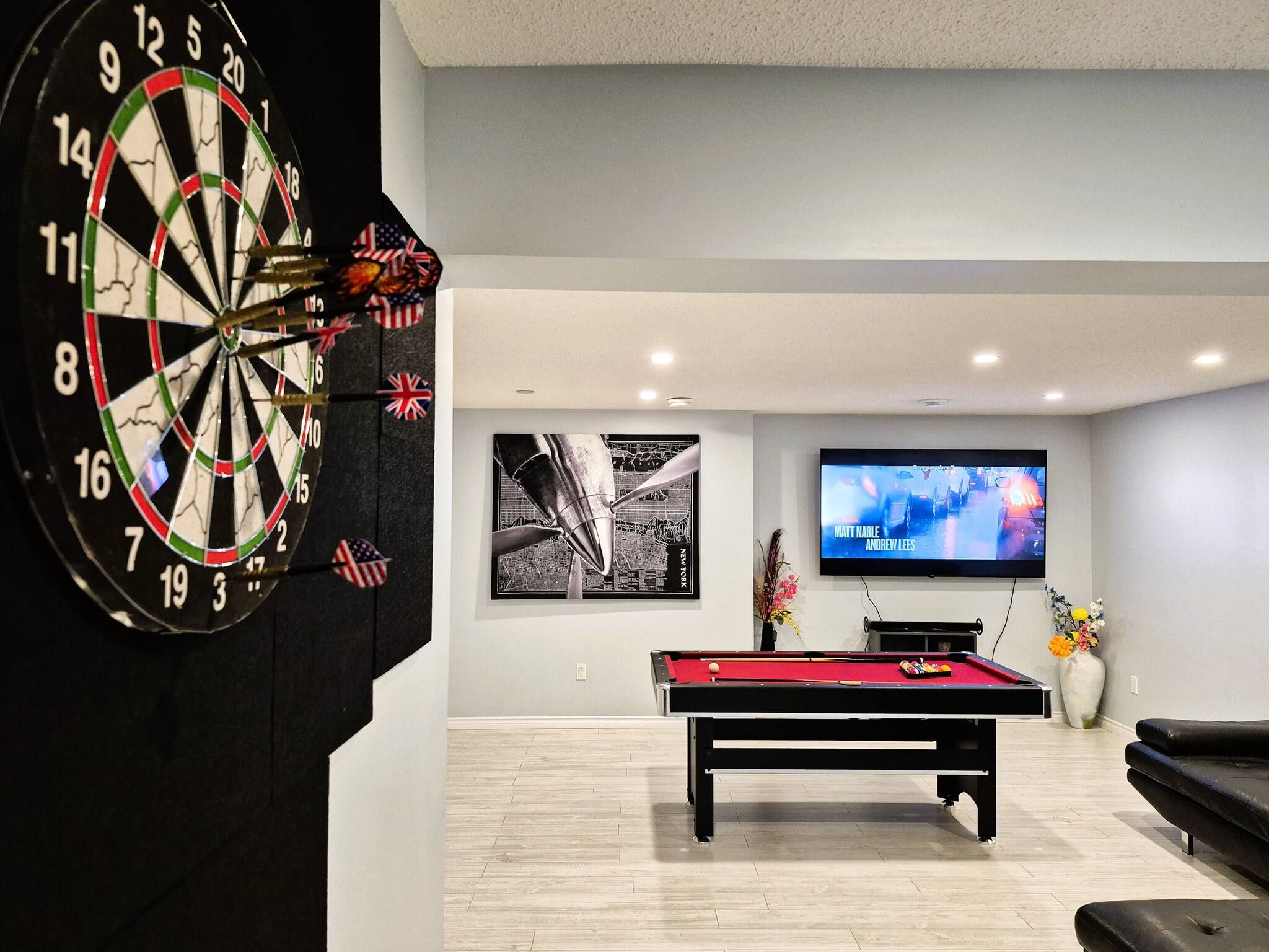 A room with a dartboard, a pool table, a television, and a framed picture on the wall.