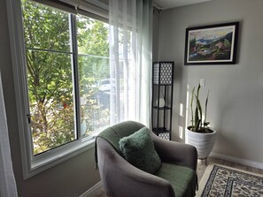 A room with a large window, a chair with a green pillow, a potted plant, and a framed painting on the wall. - Comfyspacious 3BR Home on the Park SW Edm, Near Edmonton International Airport (Edmonton)