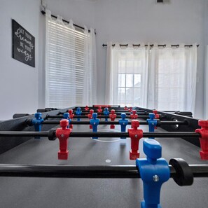 A foosball table in a room with white walls and windows with white curtains. - Modern & Cozy 3BR Home Close to Lake (Grand Prairie)