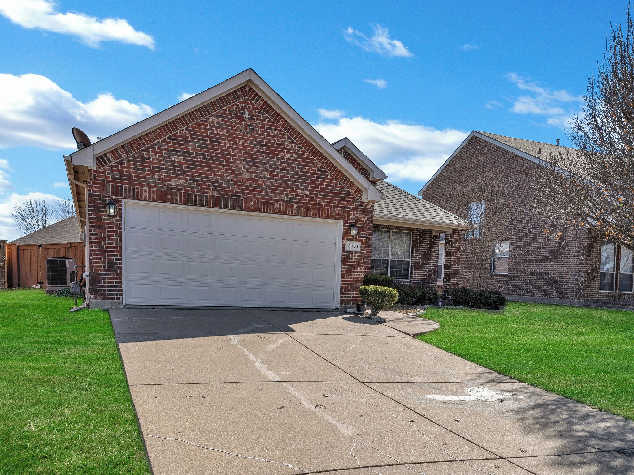 A two-story brick house with a white garage door, a small front yard, and a clear blue sky.