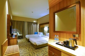 A hotel room with a large bed, a desk with a chair, a mirror, and a kitchenette area. - Al Aseel Hotel Doha (Doha)