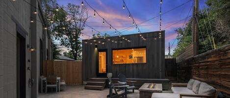 Une terrasse extérieure avec un bâtiment moderne, un espace salon et des guirlandes lumineuses.