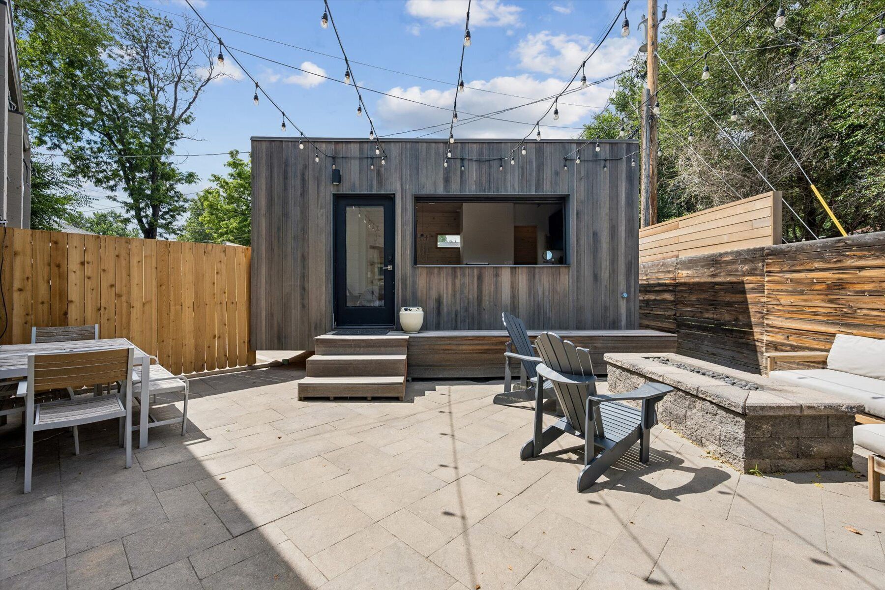 Eine moderne Terrassenanlage im Freien mit Holzdeck, einer integrierten Sitzgruppe und einer kleinen Struktur mit einer dunklen Tür und Fenstern.