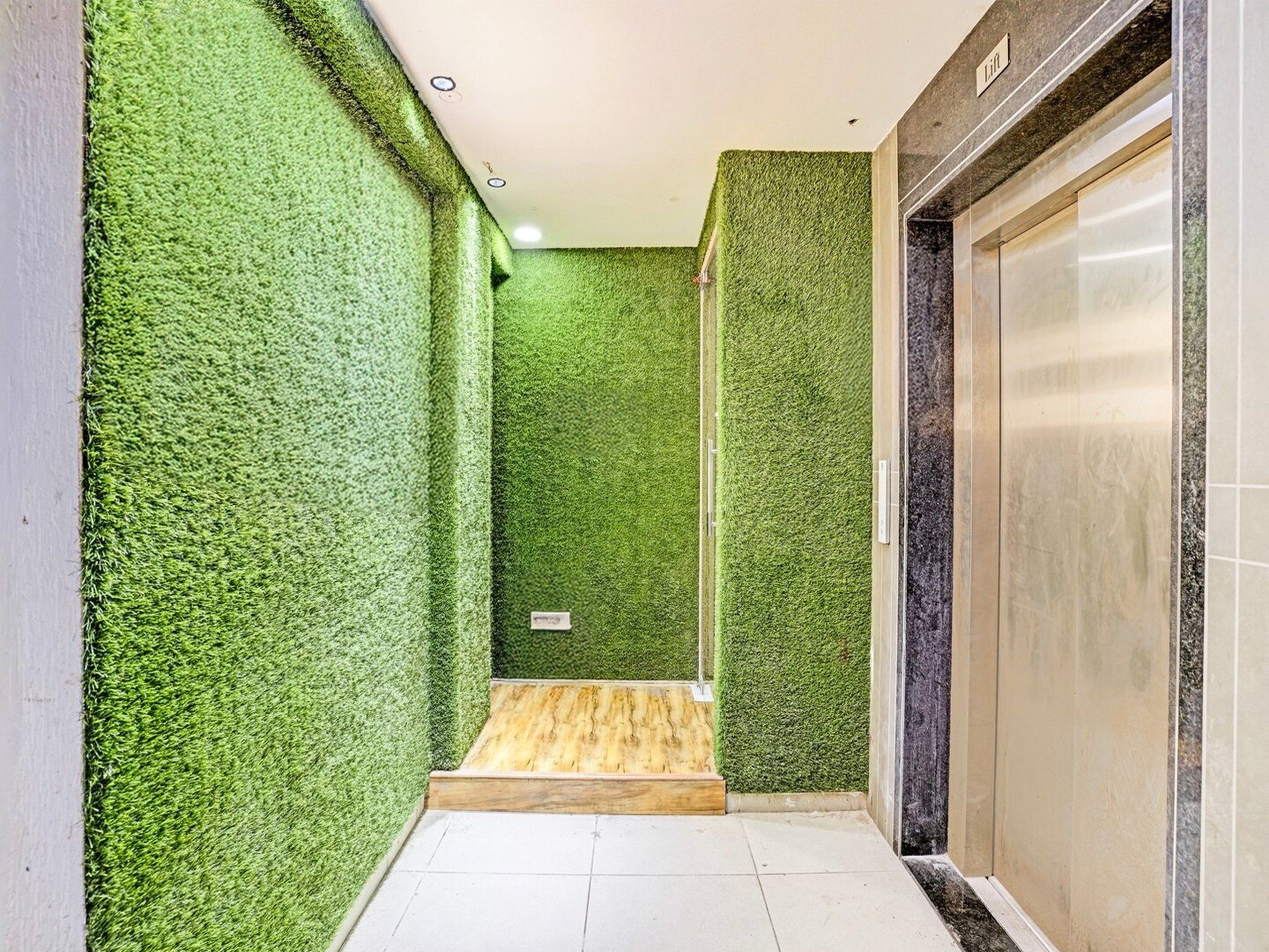 A hallway with green artificial grass walls, a wooden bench, and a closed elevator door.
