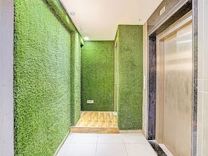 A hallway with green artificial grass walls, a wooden bench, and a closed elevator door.