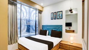 A hotel room with a large bed, a TV, a bedside table, and a window with curtains. - Classic Hotel Signature (Surat)