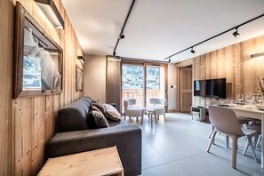 A modern interior with a sofa, dining table, chairs, and a TV. - ARKOS 202: Beautiful two-bedroom apartment for 4–5 guests in the heart of Morzine (MORZINE)