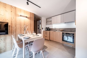 A modern kitchen with wooden cabinetry, a dining area with a white table and chairs, and a built-in oven. - ARKOS 202: Beautiful two-bedroom apartment for 4–5 guests in the heart of Morzine (MORZINE)