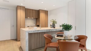 Cozinha moderna com armários de madeira, bancada de mármore e mesa de jantar de vidro com cadeiras de couro.