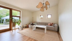 Ein geräumiges Wohnzimmer mit großem Fenster, einer Couch, einem Couchtisch und einer Pendelleuchte.