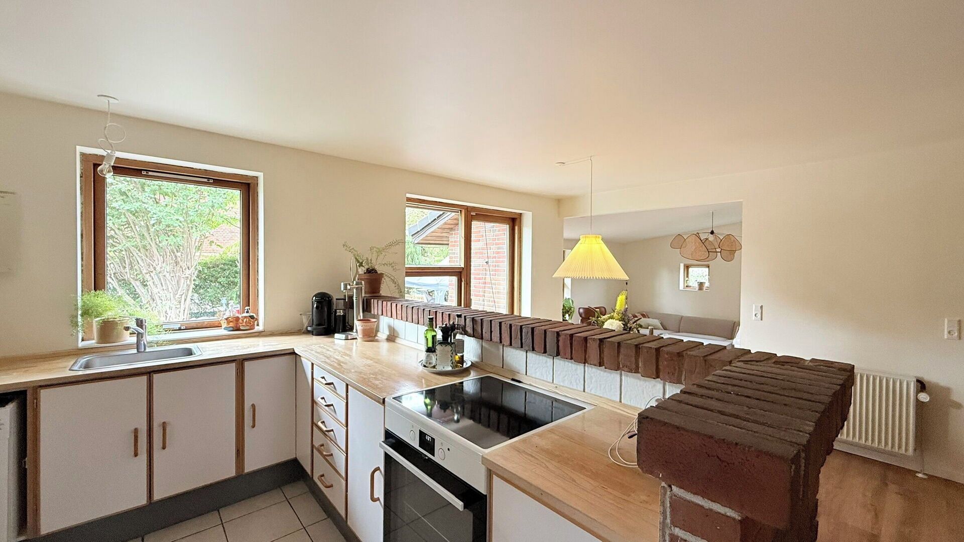 A modern kitchen with a built-in stove, a sink, and a window overlooking greenery.