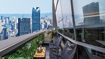 A rooftop terrace with a city view, a table with a grill, and seating.