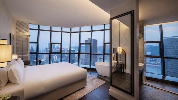 A modern hotel room with a large bed, a bathtub, and a city view through floor-to-ceiling windows. - Kongshang  River view Hotel (Chongqing)