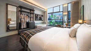 Quarto de hotel moderno com cama grande, toucador com espelho, área de estar com vista e guarda-roupa com roupas penduradas.