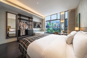 Una habitación de hotel moderna con una cama grande, un tocador con espejo, una zona de estar con vistas y un armario con ropa colgada.