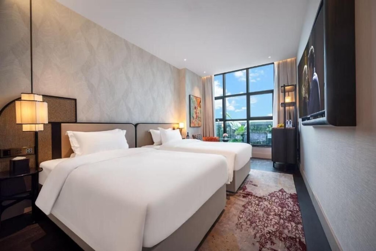 A hotel room with two beds, a large window, and a view of the outdoors.