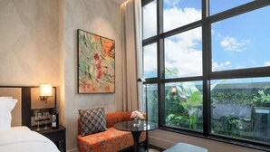 A hotel room with a bed, a sofa, a small table with a vase of flowers, and a large window offering a view of greenery. - Kongshang  River view Hotel (Chongqing)