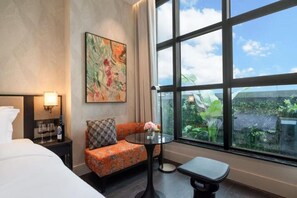 A hotel room with a bed, a sofa, a small table with a vase of flowers, and a large window offering a view of greenery. - Kongshang  River view Hotel (Chongqing)