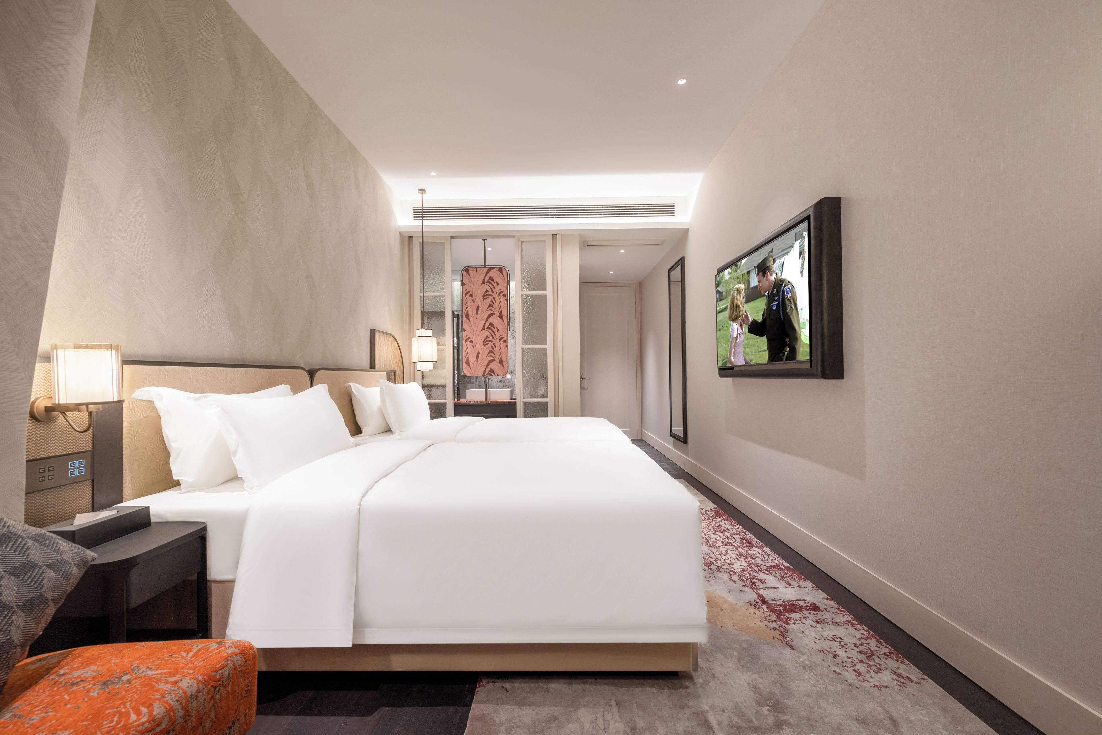 A modern hotel room with a large bed, a desk, a chair, and a television on the wall.