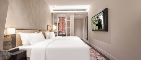A modern hotel room with a large bed, a desk, a chair, and a television on the wall.