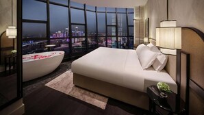 A modern bedroom with a curved window, a large bed, a bathtub, and a city view. - Kongshang  River view Hotel (Chongqing)