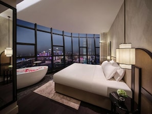 A modern bedroom with a curved window, a large bed, a bathtub, and a city view. - Kongshang  River view Hotel (Chongqing)