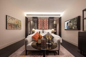 Una habitación de hotel con cama, una mesa con vasos y una botella, y obras de arte en las paredes.