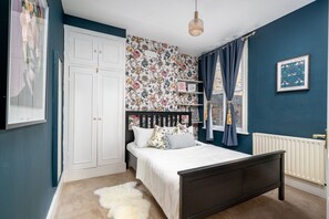 A bedroom with a bed, a wardrobe, a radiator, and a wall with floral wallpaper. - Fulham s Best-kept Secret 2 Bed Walled Garden (London)