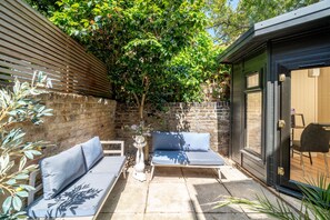 An outdoor seating area with two sofas and a table, surrounded by a brick wall and greenery. - Fulham s Best-kept Secret 2 Bed Walled Garden (London)