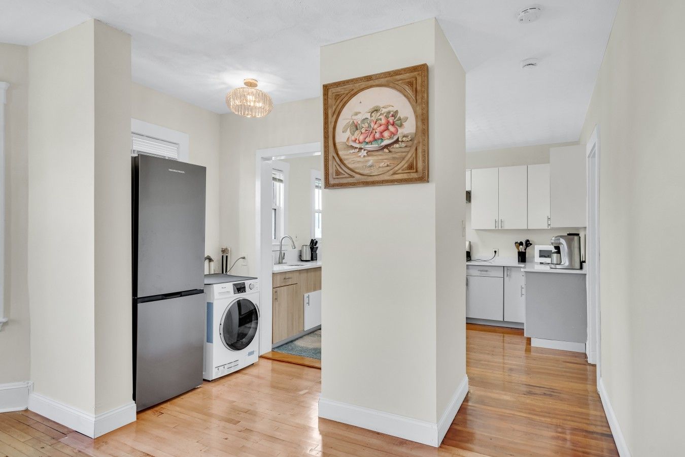 A modern kitchen with a refrigerator, washing machine, and wooden cabinets.