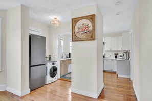A modern kitchen with a refrigerator, washing machine, and wooden cabinets. - Sunny & Spacious 2BR Apartment Near Harvard | Long Stays (Watertown)