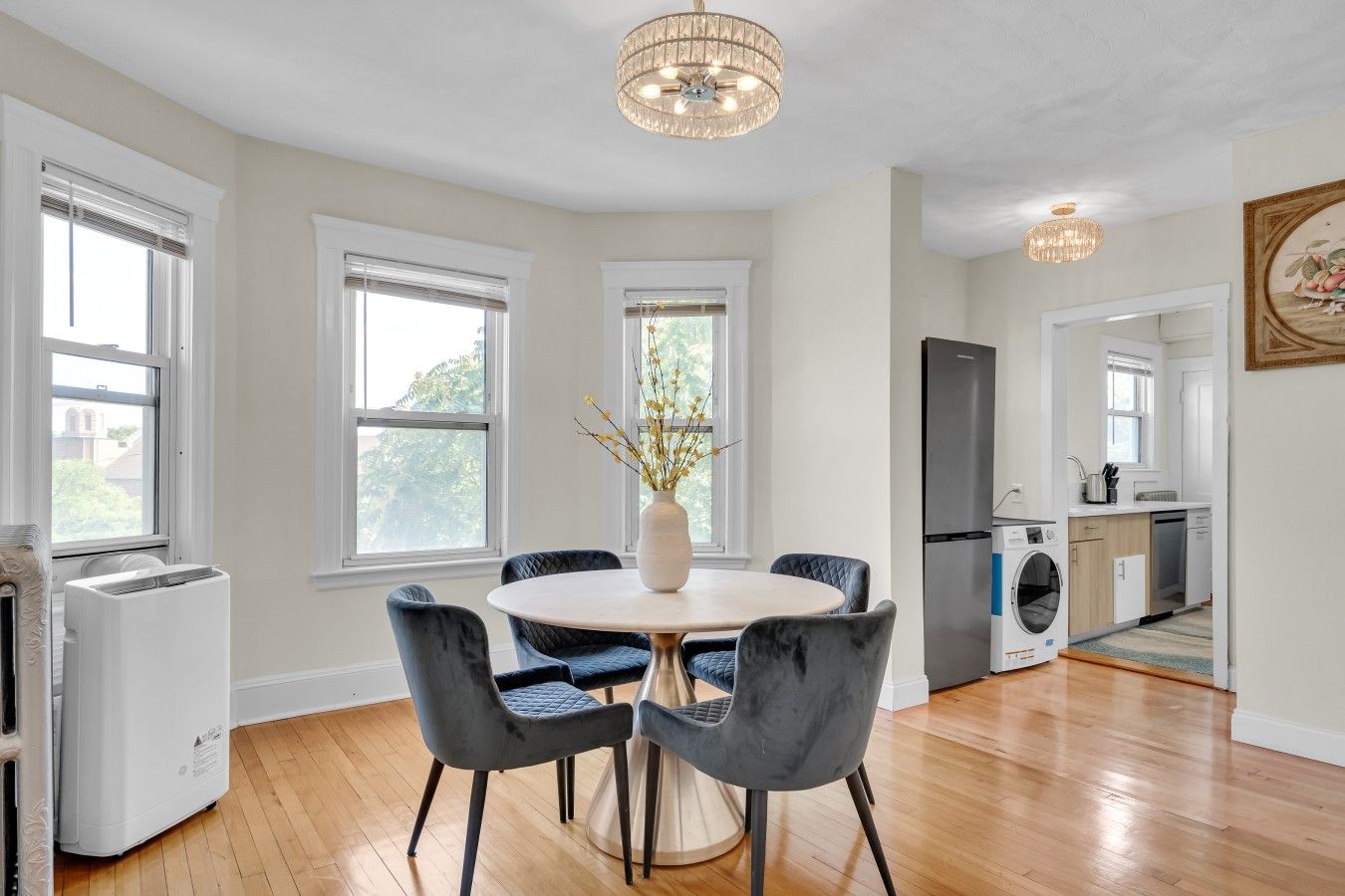 A modern kitchen with a built-in washer and dryer, a dining area with a round table and chairs, and large windows providing natural light.