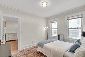 Ein Schlafzimmer mit einem Bett, einem Schminktisch, einer Stehlampe und einem Fenster mit Jalousien.