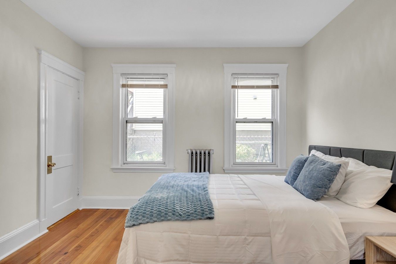 A bedroom with a bed, two windows, a radiator, and a door.