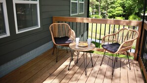 Een houten terras met twee rieten stoelen en een kleine tafel, een leuning en een huis met ramen.