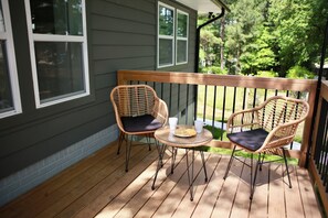 A wooden deck with two wicker chairs and a small table, a railing, and a house with windows. - Cozy Mid-Century Modern Hideaway (Durham)
