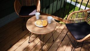 Een rieten tafel met een bord eten en twee kopjes op een houten terras.