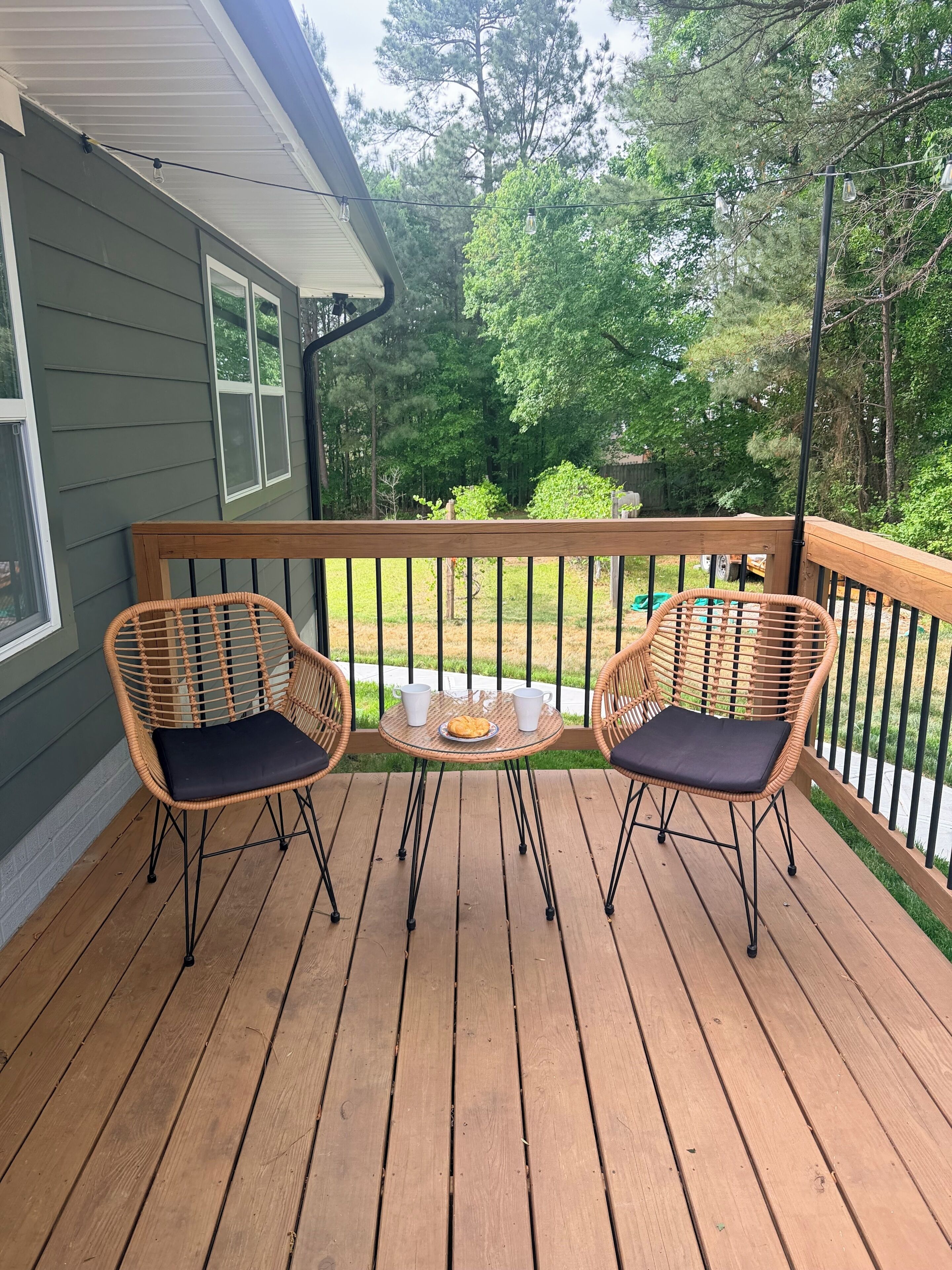 A wooden deck with two wicker chairs and a small table, surrounded by a railing.