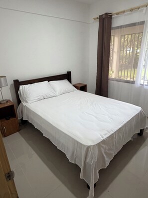 A single-bed room with a wooden headboard, a bedside table, and a window with curtains. - Peaceful 2-bedroom house in charming Ulima, San Carlos, Alajuela Province (Alajuela Province)