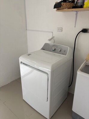 Lavadora de carga frontal blanca con panel de control, conectada a un enchufe.