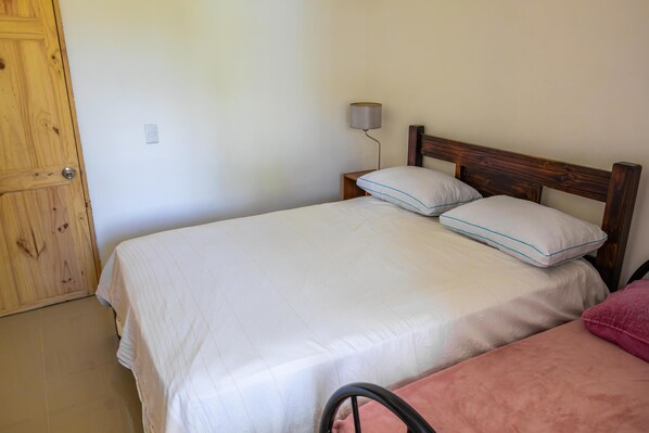 A single bed with a wooden headboard in a room with a plain wall and a door.