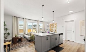 A modern kitchen with a central island, pendant lighting, and a view to the outside. - Secord Wellness Retreat | Sauna | Yard | Near WEM (Edmonton)